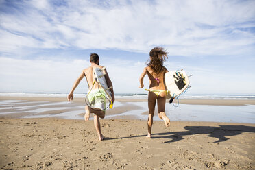 Couple carrying surfboards running on the beach - ABZF01723