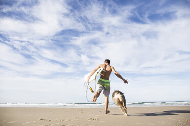 Mann mit Surfbrett läuft mit Hund am Strand - ABZF01730