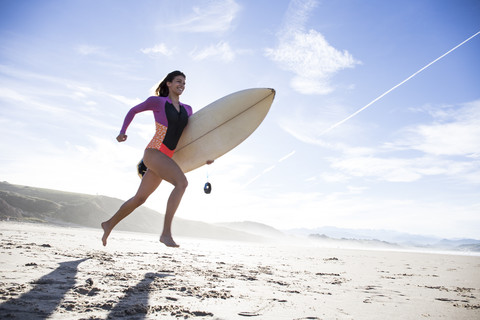 Woman carrying surfboard running on the beach stock photo