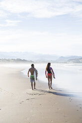 Couple carrying surfboards walking on the beach - ABZF01737