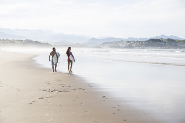 Couple carrying surfboards walking on the beach - ABZF01738