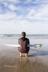 Mann mit Surfbrett am Strand hockend - ABZF01740