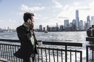 USA, Geschäftsmann am Mobiltelefon in New Jersey am Wasser mit Blick auf Manhattan - UUF09691