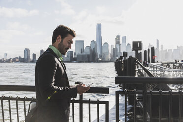 USA, businessman using cell phone at New Jersey waterfront with view to Manhattan - UUF09692