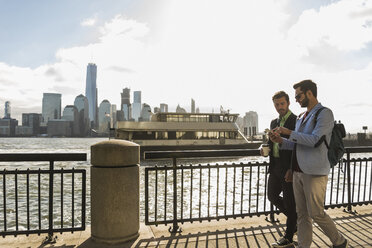 USA, two businessmen walking at New Jersey waterfront with view to Manhattan - UUF09695