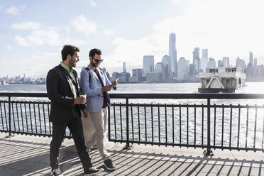 USA, two businessmen walking at New Jersey waterfront with view to Manhattan - UUF09696