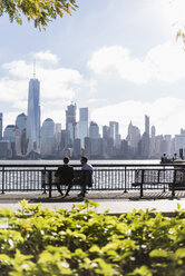 USA, zwei Geschäftsleute sitzen auf einer Bank am Ufer von New Jersey mit Blick auf Manhattan - UUF09704