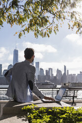 USA, man using laptop at New Jersey waterfront with view to Manhattan - UUF09706