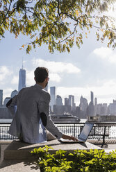 USA, Mann benutzt Laptop am Hafen von New Jersey mit Blick auf Manhattan - UUF09706