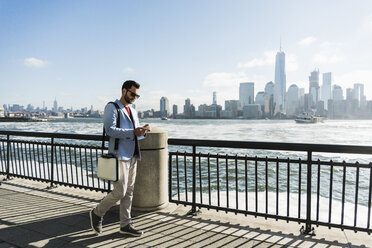 USA, Mann mit Mobiltelefon am Hafen von New Jersey mit Blick auf Manhattan - UUF09708