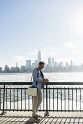 USA, Mann mit Mobiltelefon am Hafen von New Jersey mit Blick auf Manhattan - UUF09709