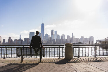 USA, man sitting on bench at New Jersey waterfront with view to Manhattan - UUF09712