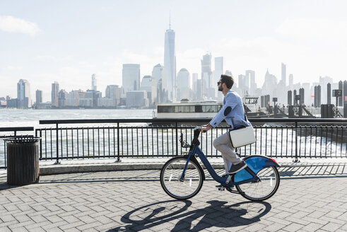 USA, Mann auf Fahrrad am Hafen von New Jersey mit Blick auf Manhattan - UUF09717