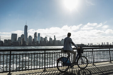 USA, Mann auf Fahrrad am Hafen von New Jersey mit Blick auf Manhattan - UUF09718