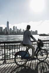 USA, Mann auf Fahrrad am Hafen von New Jersey mit Blick auf Manhattan - UUF09721