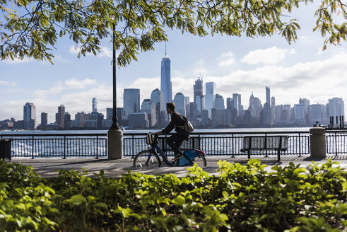 USA, Mann auf Fahrrad am Hafen von New Jersey mit Blick auf Manhattan - UUF09726