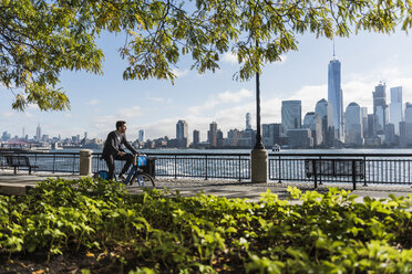 USA, Mann auf Fahrrad am Hafen von New Jersey mit Blick auf Manhattan - UUF09727