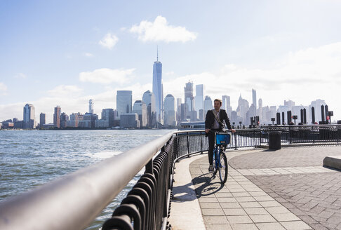USA, Mann auf Fahrrad am Hafen von New Jersey mit Blick auf Manhattan - UUF09728