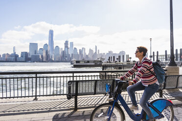 USA, woman on bicycle at New Jersey waterfront with view to Manhattan - UUF09731