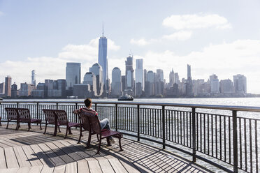 USA, Frau sitzt auf einer Bank am Ufer von New Jersey mit Blick auf Manhattan - UUF09733