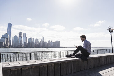 USA, man using tablet at New Jersey waterfront with view to Manhattan - UUF09736