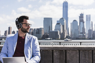 USA, Mann mit Kopfhörern und Tablet am Ufer von New Jersey mit Blick auf Manhattan - UUF09750