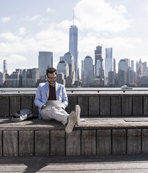 USA, man wearing headphones using tablet at New Jersey waterfront with view to Manhattan - UUF09751