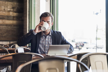 Businessman drinking coffee and using tablet in a cafe - UUF09755