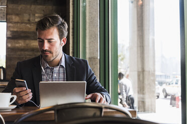 Geschäftsmann mit Tablet und Mobiltelefon in einem Café - UUF09756