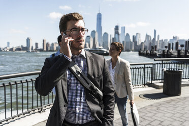 USA, Geschäftsmann am Mobiltelefon in New Jersey am Wasser mit Blick auf Manhattan - UUF09760