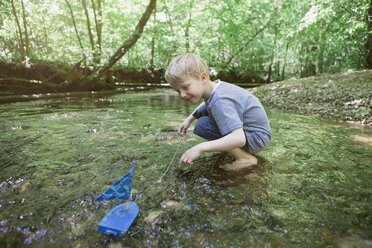 Boy playing with a toy boat in a forest brook - RBF05527