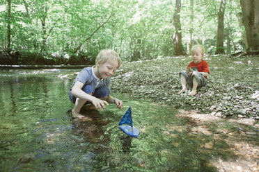 Two boys playing with a toy boat in a forest brook - RBF05528