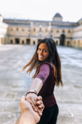 Happy young woman holding hand on urban square - MGOF02750