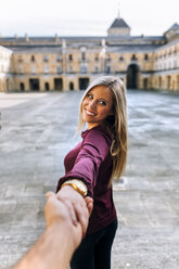 Happy young woman holding hand on urban square - MGOF02751