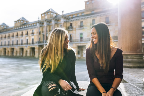 Zwei lächelnde junge Frauen unterhalten sich auf einem städtischen Platz, lizenzfreies Stockfoto