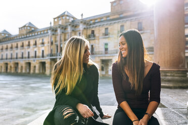 Zwei lächelnde junge Frauen unterhalten sich auf einem städtischen Platz - MGOF02752