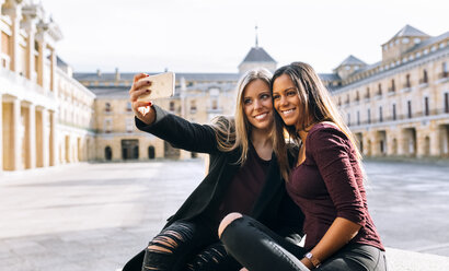 Zwei lächelnde junge Frauen auf einem städtischen Platz machen ein Selfie - MGOF02754