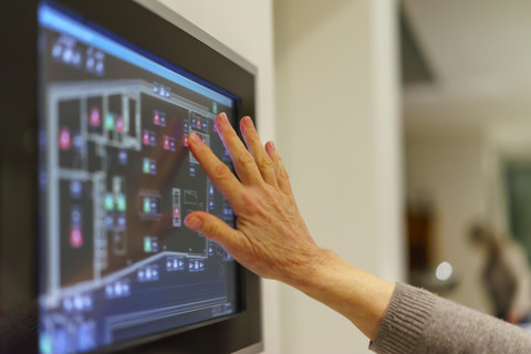 Die Hand einer älteren Frau berührt die Anzeigetafel der Haustechnik, lizenzfreies Stockfoto