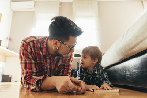 Vater und Sohn liegen mit einem Buch auf dem Boden, lizenzfreies Stockfoto