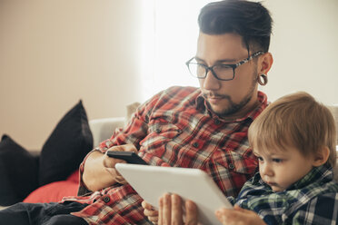 Father and son on couch using tablet and cell phone - ZEDF00501