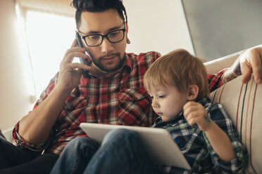 Father and son on couch using tablet and cell phone - ZEDF00503