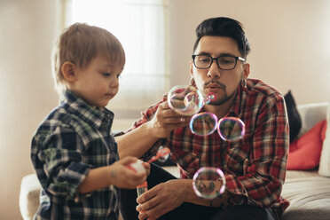 Father and son blowing soap bubbles at home - ZEDF00504