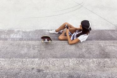 Junge Frau mit Skateboard schaut auf ihr Handy - MGOF02770