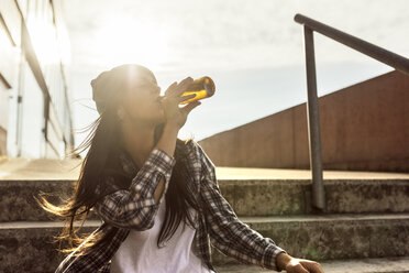 Young woman sitting on stairs drinking a beer from the bottle - MGOF02776