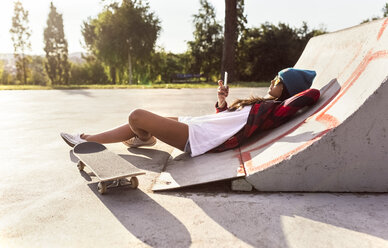 Junge Frau mit Skateboard und Mobiltelefon in einem Skatepark - MGOF02781