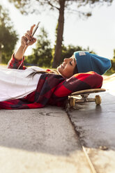 Young woman lying on skateboard looking at cell phone - MGOF02783