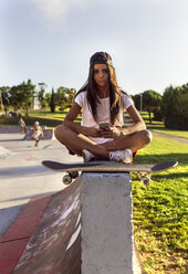 Junge Frau mit Skateboard und Mobiltelefon in einem Skatepark - MGOF02784