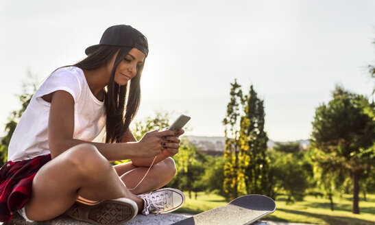 Junge Frau mit Skateboard schaut auf ihr Handy - MGOF02785