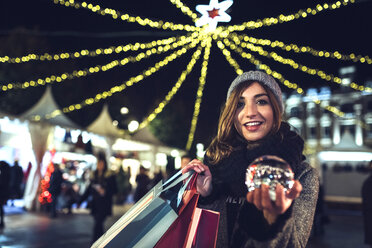 Porträt einer glücklichen Frau mit Tüten und Schneekugel auf dem Weihnachtsmarkt - DAPF00529