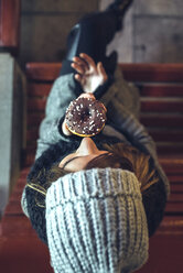 Frau sitzt auf Bank und isst Donut mit Schokoladenglasur, Ansicht von oben - DAPF00535